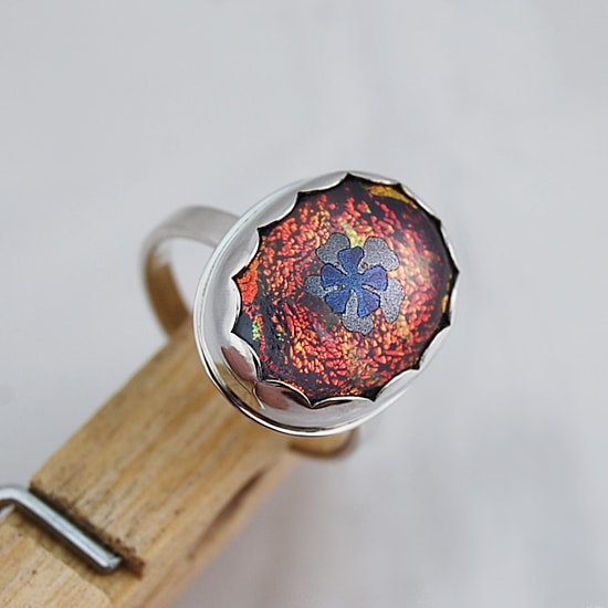 Red dichroic glass with a lavender columbine set in a sterling silver scalloped bezel on a sturdy sterling silver ring size 7.5
